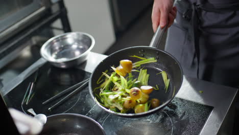 chef tossing veggies in skillet while frying