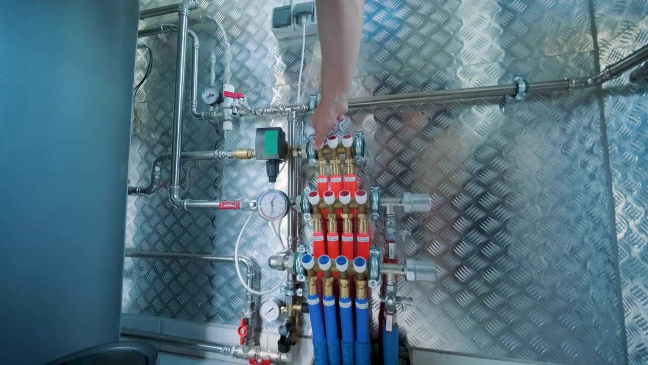 Tecnico che regola le valvole su un sistema collettore di riscaldamento industriale