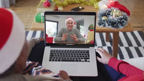 African-american-mother-and-daughter-using-laptop-for-christmas-video-call-with-man-on-screen