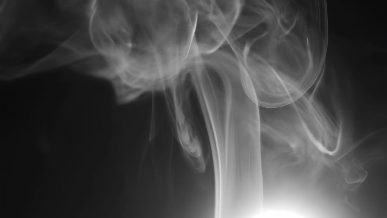 Fumo pallido si arriccia e si diffonde su uno sfondo scuro e vuoto, con volute stratificate, un bagliore morbido vicino al bordo inferiore destro e una foschia più densa che si addensa vicino alla parte superiore.