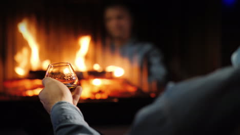 a man drinks brandy by the fireplace his face is reflected in the glass of the furnace