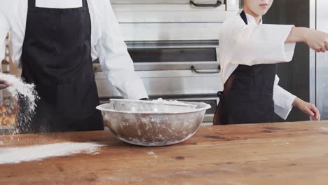 Diverse-bakers-working-in-bakery-kitchen,-pouring-flour-on-counter-in-slow-motion