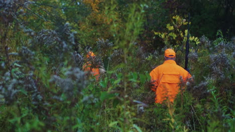 Three-men-in-blaze-orange-safety-vests-carrying-guns-while-hunting-together