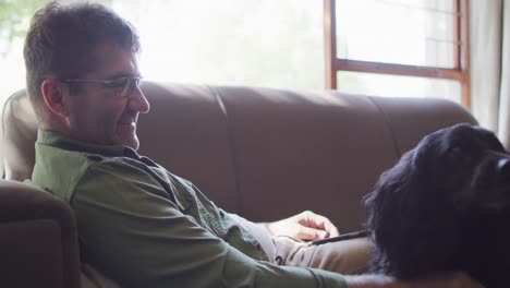 Caucasian-man-sitting-on-sofa,-petting-dogs,-smiling-at-home