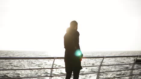 Male-silhouette-taking-out-smartphone-out-of-the-pocket-during-exercising-on-the-dock-near-the-seaside.-Sport-and-recreation.