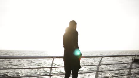 male silhouette taking out smartphone out of the pocket during exercising on the dock near the seaside. sport and recreation.