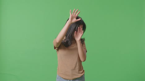 얼굴에 이 있는 폭력의 희생자인 젊은 아시아 여성은 스튜디오의 녹색 스크린 배경에서 손으로 방어하는 몸짓을 하고 두려워합니다.