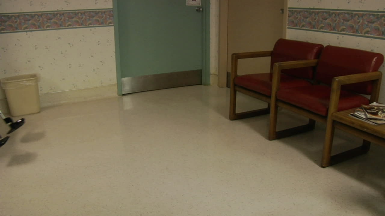 una enfermera conduce una silla de ruedas vacía por el vestíbulo de un hospital