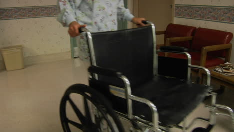 a nurse wheels an empty wheelchair through a hospital lobby