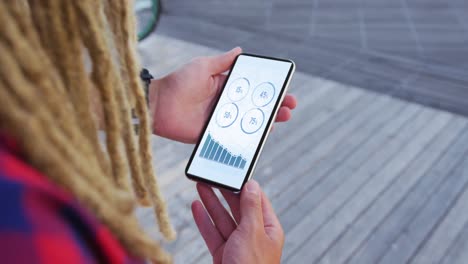 hands of caucasian man with dreadlocks using smartphone with statistics on screen