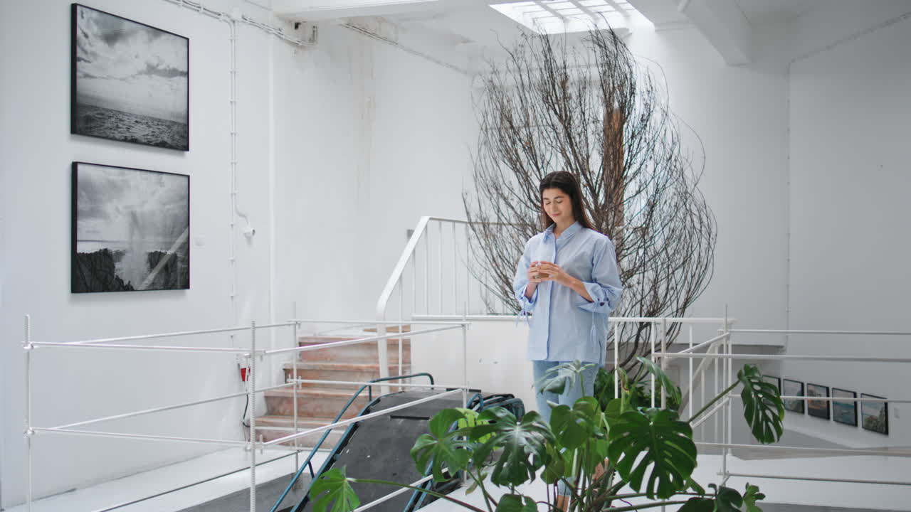 женщина, идущая по современному офисному залу. успешная бизнесменка, держащая стакан с водой.