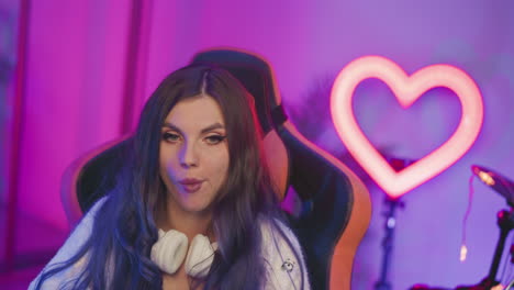 young female artist seated on gaming chair eating popcorn under vibrant purple lighting, with glowing heart-shaped neon light and drums in background