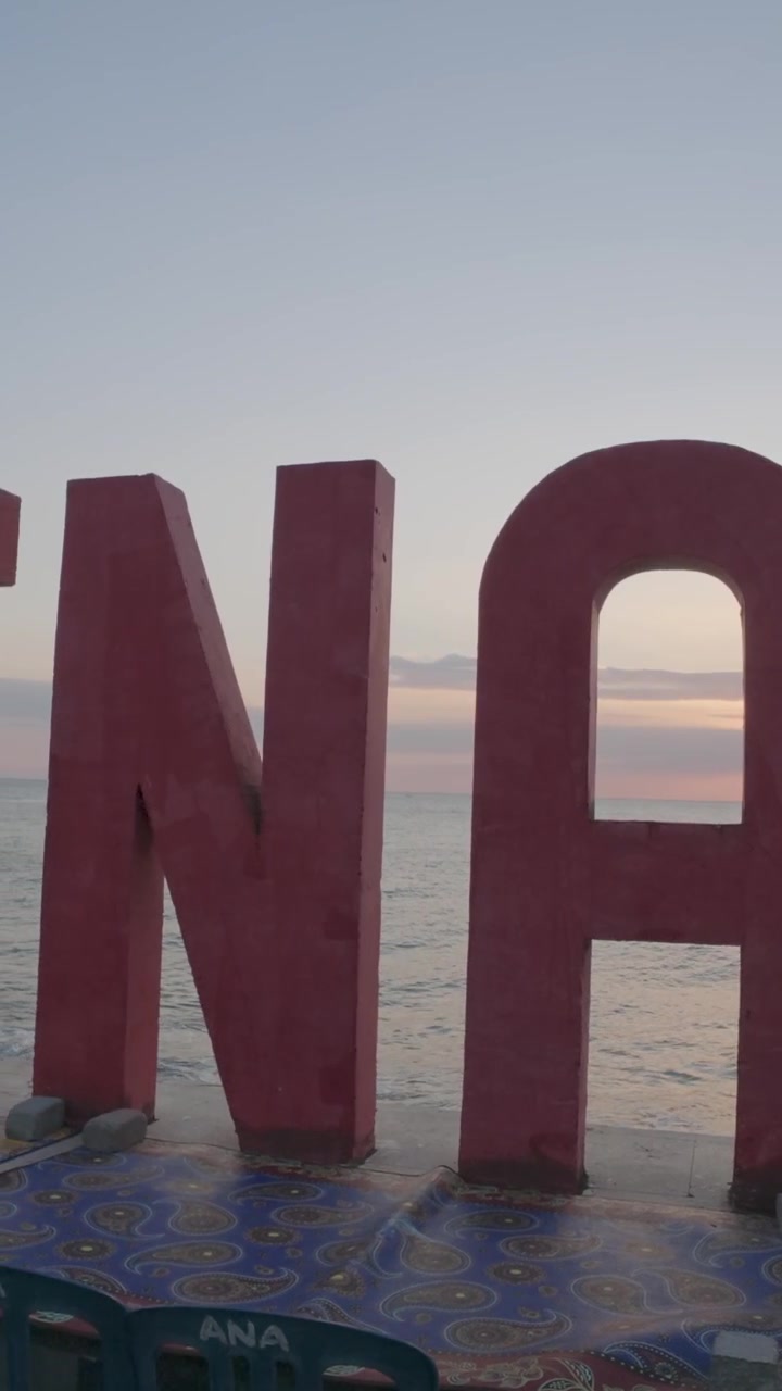 Grandi lettere rosse che compongono la parola Open su una spiaggia al tramonto