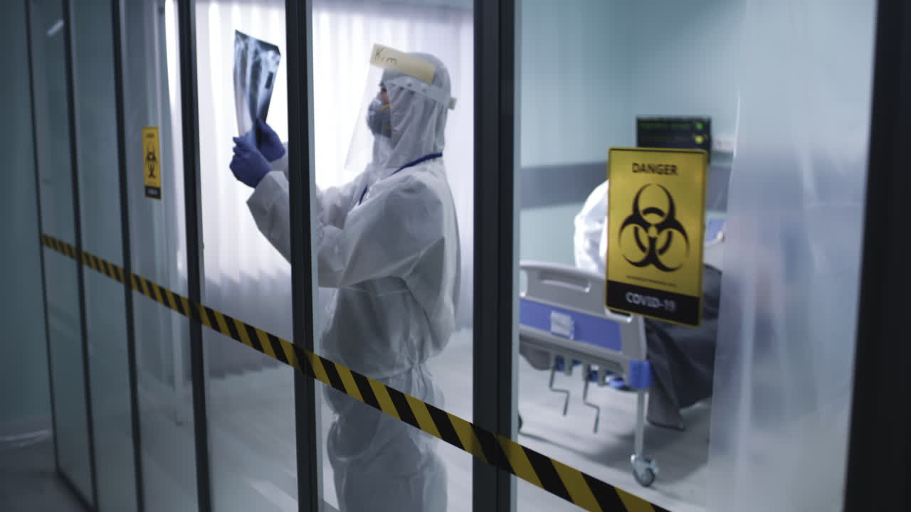 A medical professional in full PPE examines an X-ray scan in a hospital