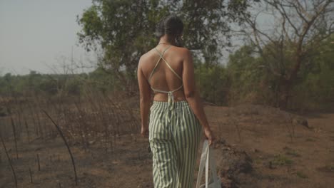 mujer camina a cámara lenta por el bosque con sus gafas de sol en una mano y su maleta en la otra - un momento sereno y pintoresco en un día soleado