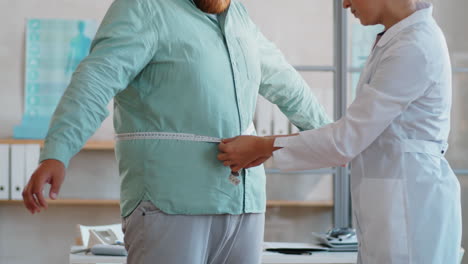 médico midiendo la cintura de un hombre con sobrepeso en la clínica