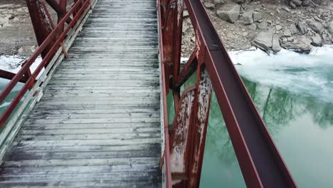 close up of rusty old red footbridge over icy river