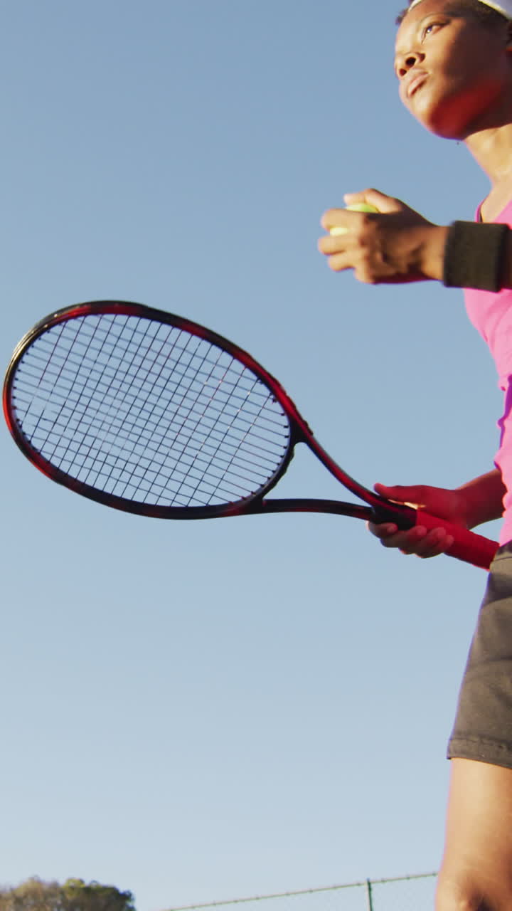 video de ángulo bajo de una tenista afroamericana enfocada sosteniendo una raqueta y golpeando la pelota