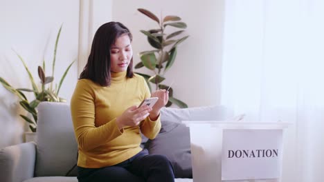 Asian-woman-pressing-phone-using-a-credit-card-to-pay-online-to-reserve-donation-box-delivery