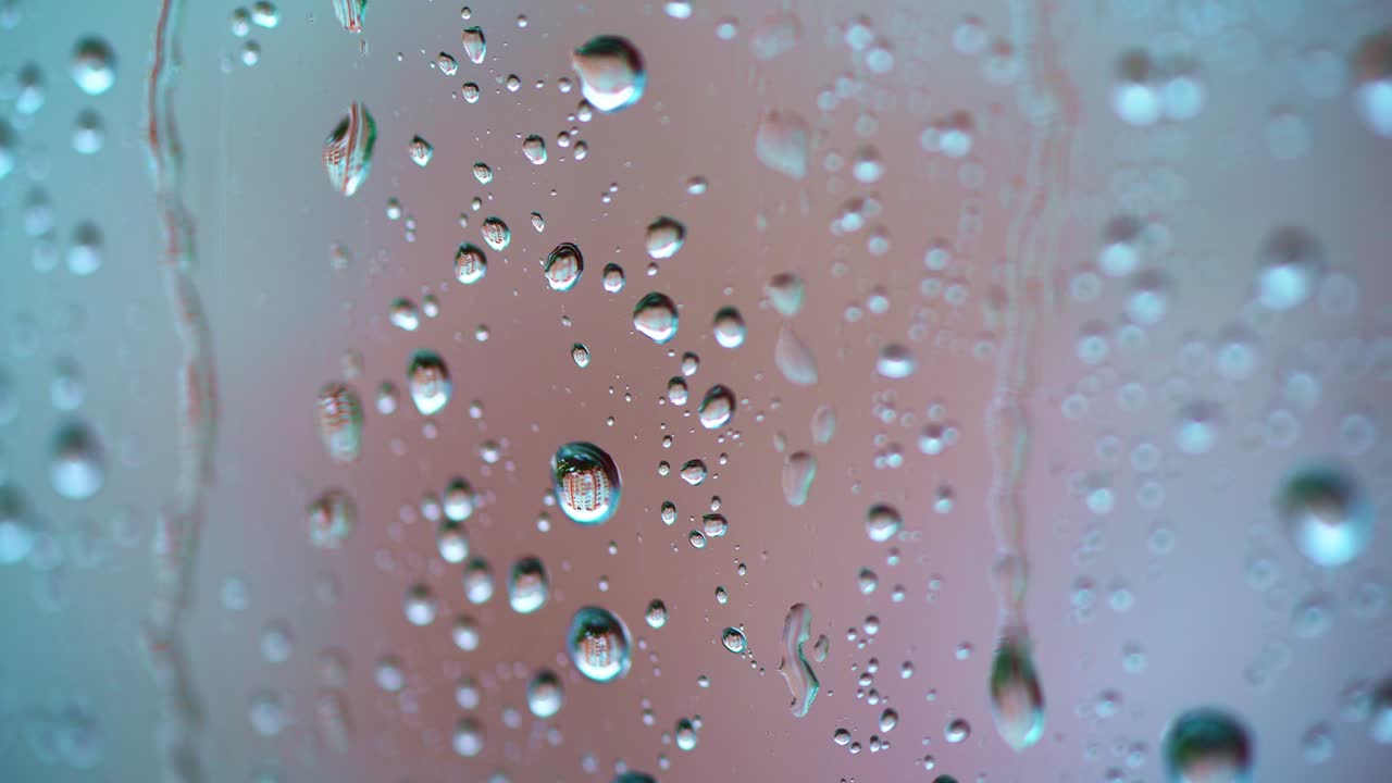 Big raindrops on glass window background. Slow motion of water drops flowing on the glass in a rainy weather. Macro shot.