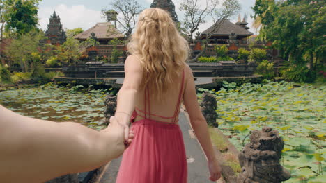 Pareja-De-Viajes-Tomados-De-La-Mano-Mujer-Feliz-Novio-Líder-Explorando-El-Templo-De-Saraswati-Divirtiéndose-Turismo-Cultura-De-Bali-Indonesia