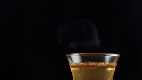 a close-up shot of a hot beverage steaming in a glass against a black background
