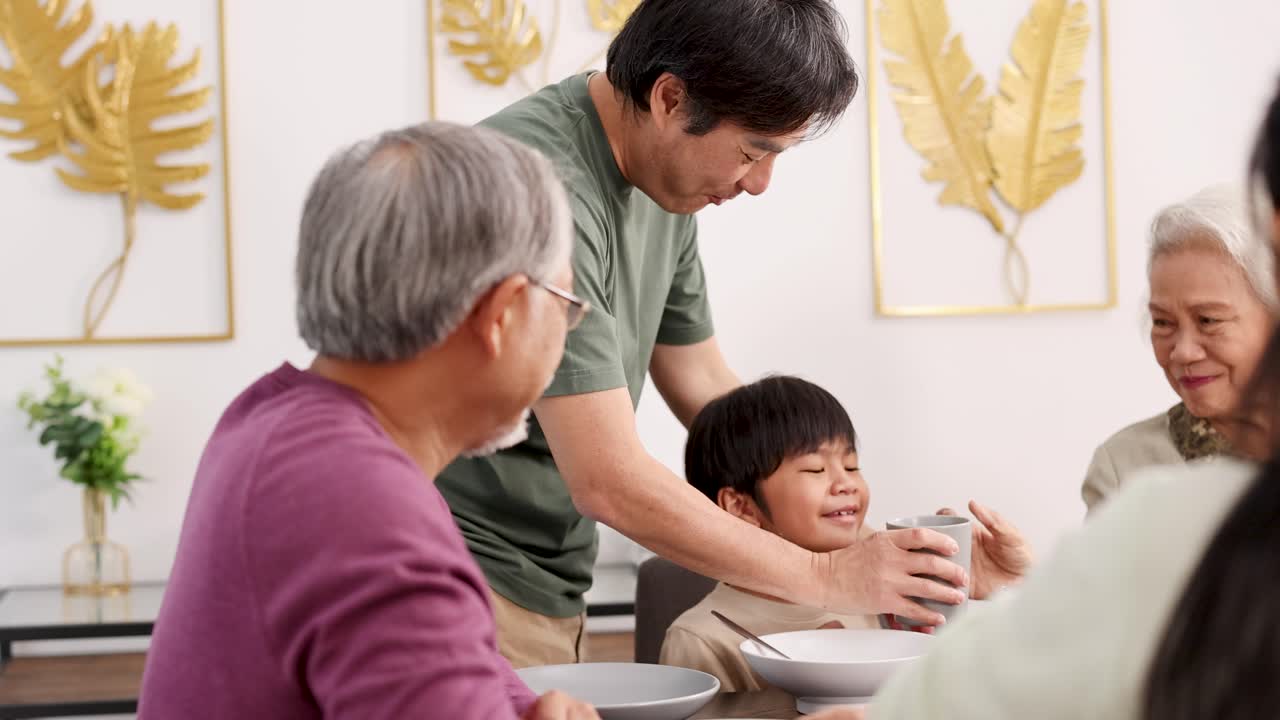 A family gathers around a dining table, sharing food and laughter in a warmly lit room