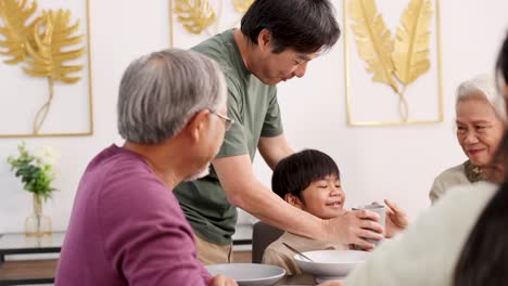 a family gathers around a dining table, sharing food and laughter in a warmly lit room