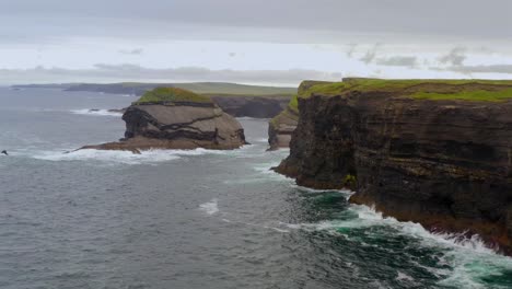 static aerial shot of a rugged cliff face and a rocky islet off the coast of kilkee cliffs in county clare, showcasing dramatic coastal features