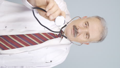 Vertical-video-of-Old-doctor-listening-to-camera-with-stethoscope.