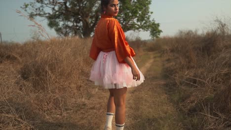 Girl-in-a-red-shirt-and-a-pink-skirt-walks-towards-a-tree-and-looks-back-into-the-camera-as-she's-walking