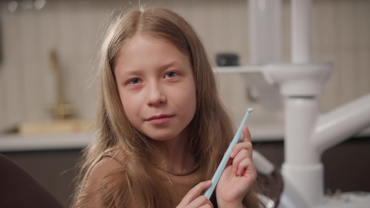 Close up of young girl holding dental tool in orthodontic clinic setting soft lighting calm expression focused on subject dental equipment visible background