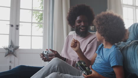 Happy-pre-teen-boy-and-his-middle-aged-father-sitting-on-the-floor-in-the-living-room-laughing-and-playing-video-games-together,-close-up