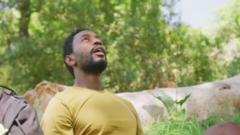 happy african american man with backpack sitting in park, slow motion