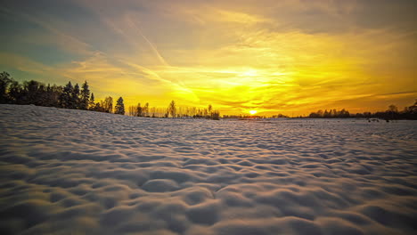 Dramatic-golden-sunset-time-lapse---sun-dips-behind-the-horizon-beyond-a-field-of-snow-and-trees