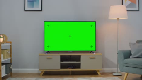 zoom out shot of a tv with horizontal green screen mock up. cozy living room at day time with a chair and lamps turned on at home.