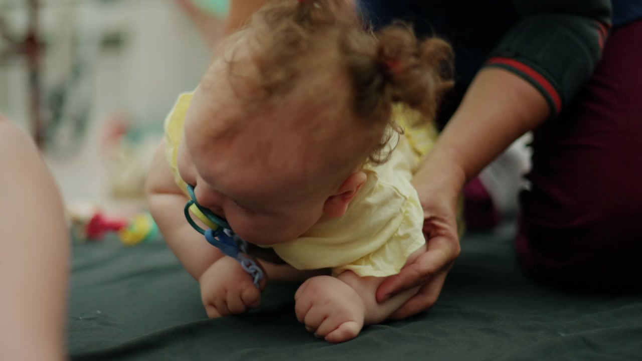 Baby with curly hair and pacifier playing upside down, experiencing joy and bonding with an adult. Childhood development concept
