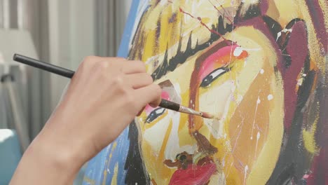 cerca de una mano sosteniendo un pincel de colores mixtos y pintando el rostro de una niña en el lienzo