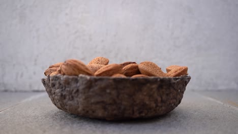 almond nuts in shell falling on wooden bowl