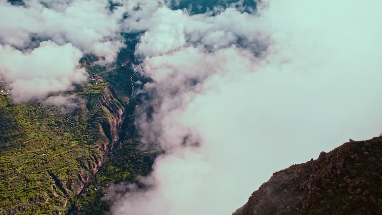 Drone flight over Colca Canyon, panning through clouds, revealing Malata-Cos&ntilde;irhua village in spring, post-rain cloudy day