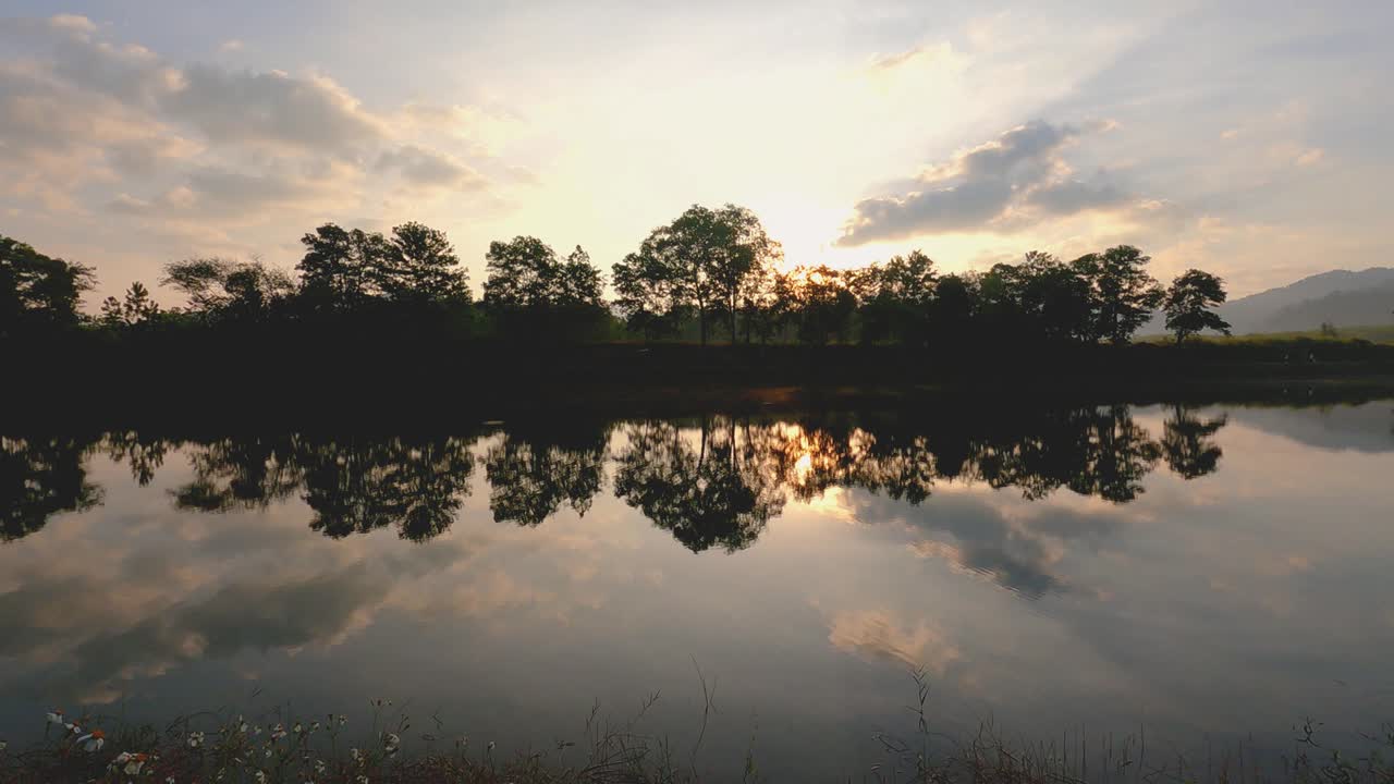 hermoso amanecer cielo en la mañana de primavera en el lago. brillo del sol sobre el cielo azul y el reflejo de los árboles y el color naranja del sol de la mañana en la superficie del agua. nubes que se mueven rápidamente en el amplio espacio.
