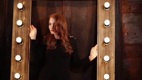 woman in black dress posed in front of a wooden frame with lights.