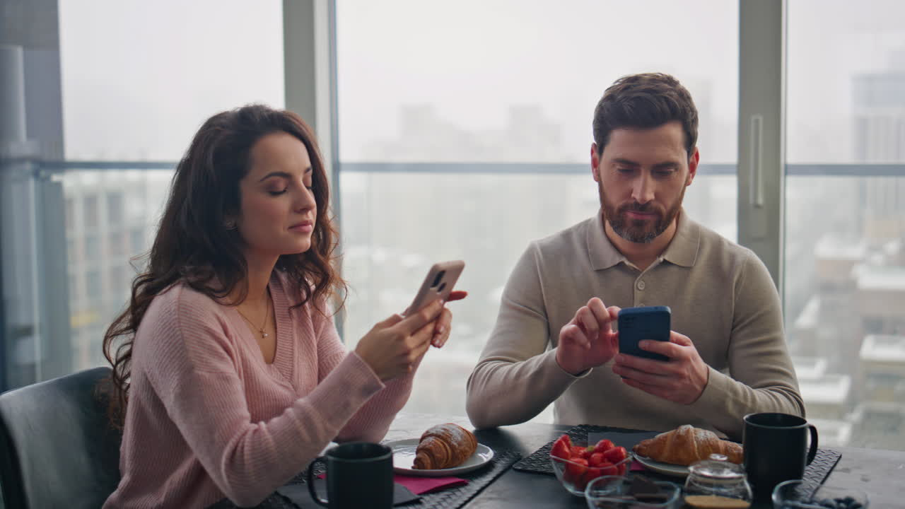 una pareja adicta a internet se ignora la una a la otra sentada en una casa de paisaje urbano sombrío.