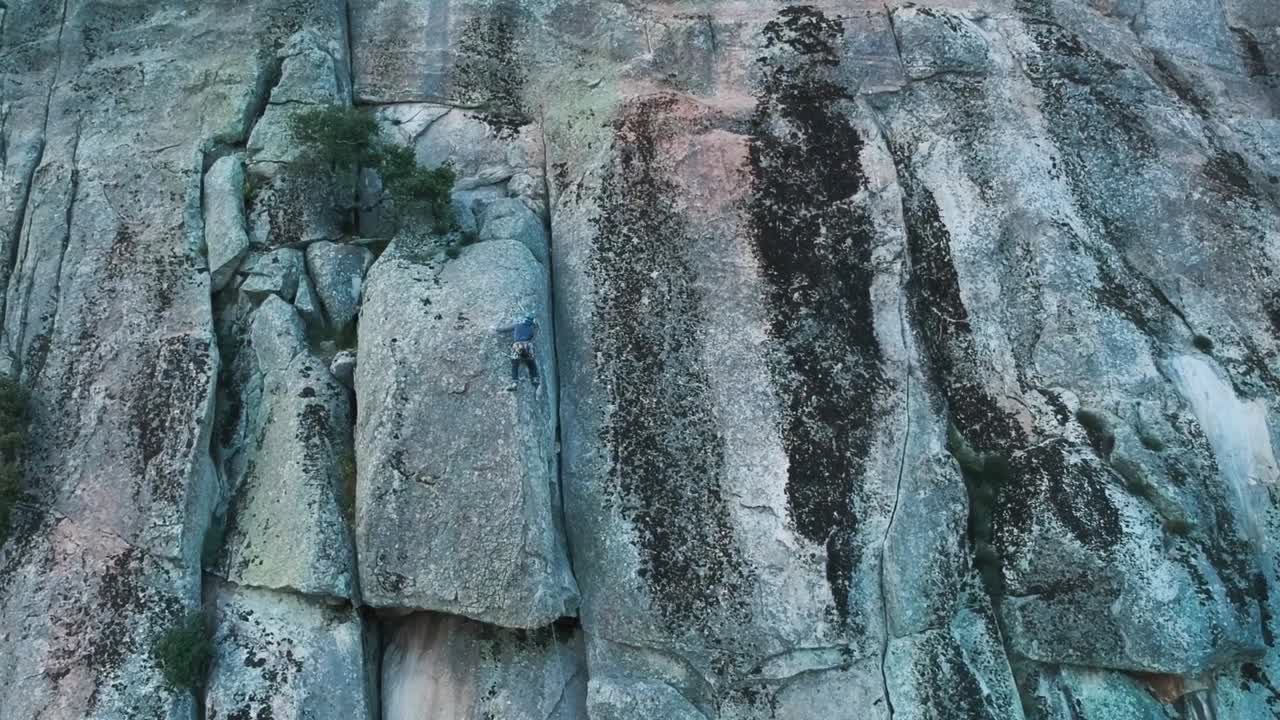 A tiny climber is stuck on a tricky step on a granite wall