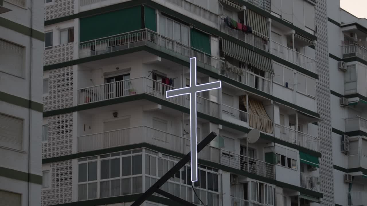 cruz iluminada entre edificios al anochecer