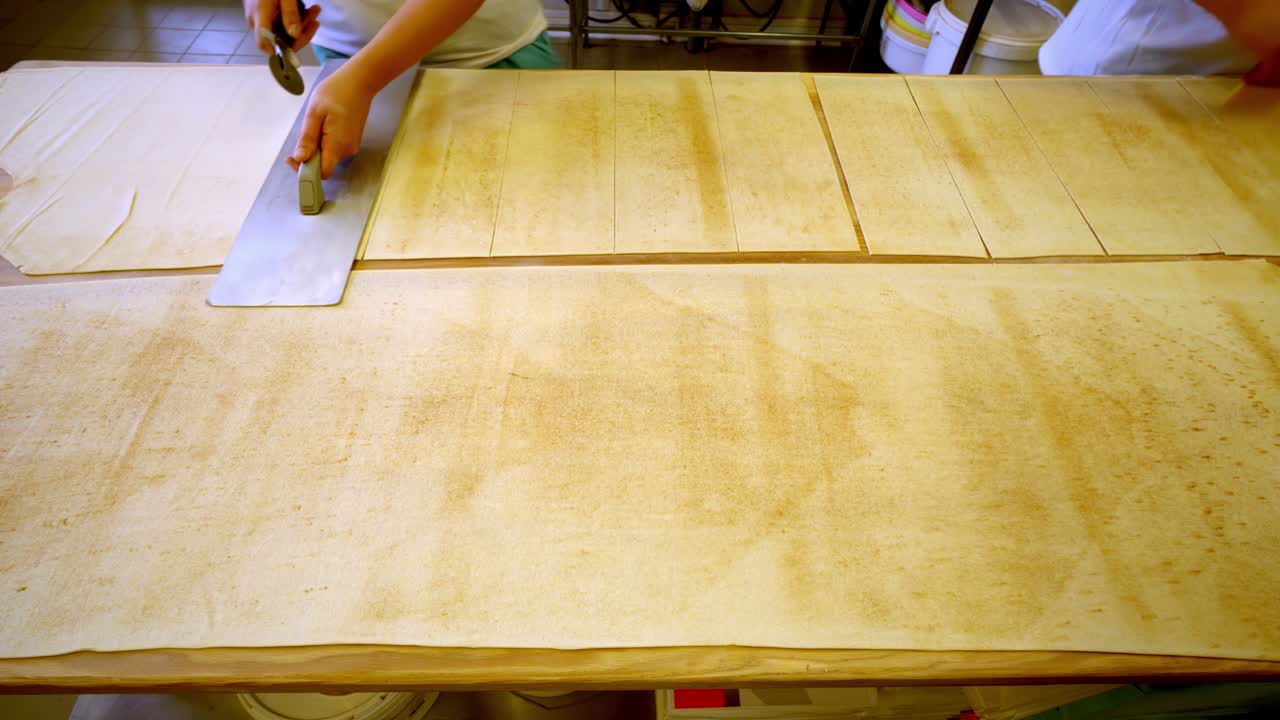 Person carefully cuts pasta dough sheets in kitchen, focus on hands