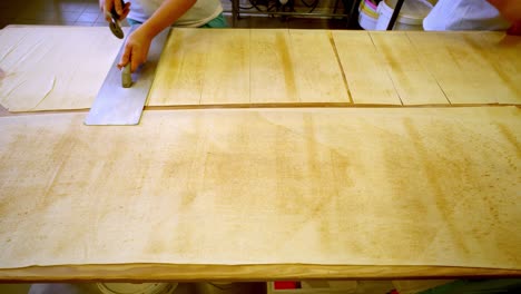 person carefully cuts pasta dough sheets in kitchen, focus on hands