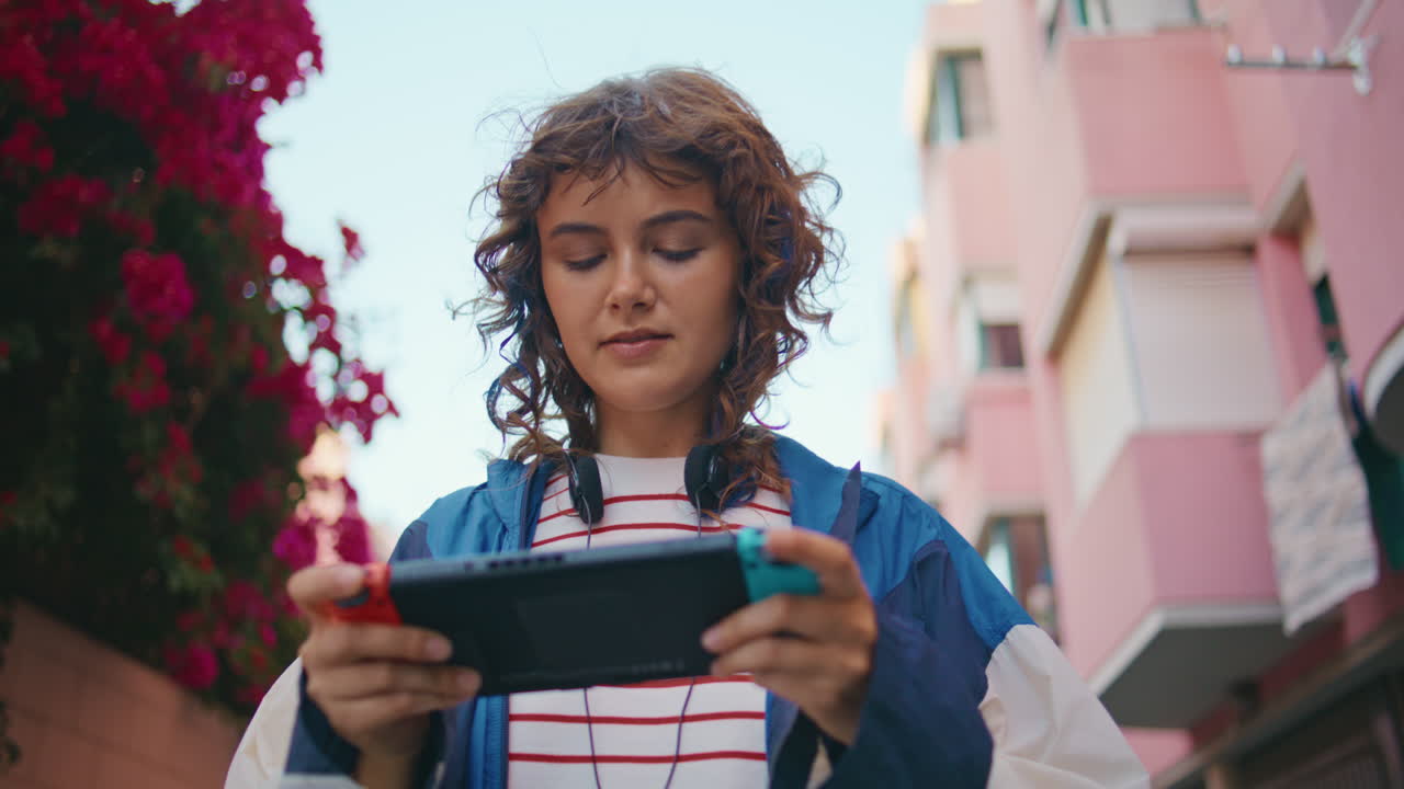 una mujer joven jugando a la consola nintendo switch caminando por la calle de verano de cerca