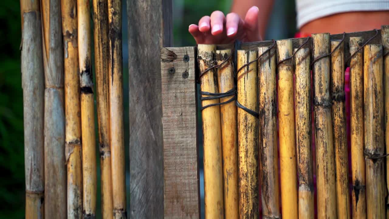 la mano de una mujer abriendo lentamente una puerta de bambú de madera en el lago atitlan, guatemala