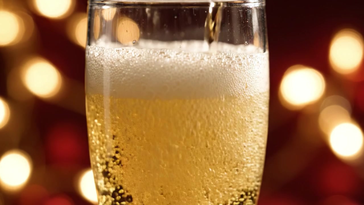 Una bevanda frizzante viene versata in un bicchiere, catturando l'effervescenza e le bollicine vivaci su uno sfondo di luci calde e brillanti, creando un'atmosfera festosa.